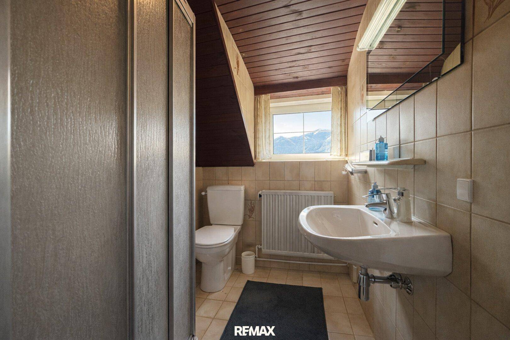 Badezimmer im Dachgeschoss mit Dusche, Waschbecken und Holzdecke, gefliest.