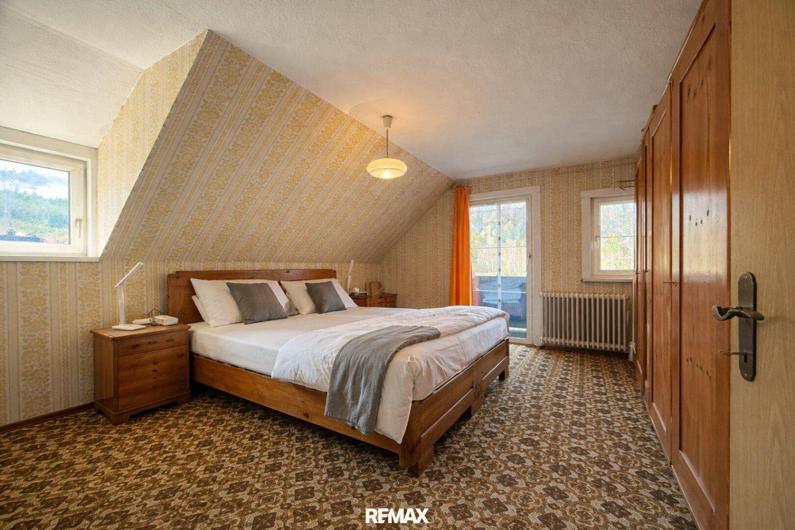 Schlafzimmer im Dachgeschoss mit Teppichboden, Holzschrank und Zugang zum Balkon.