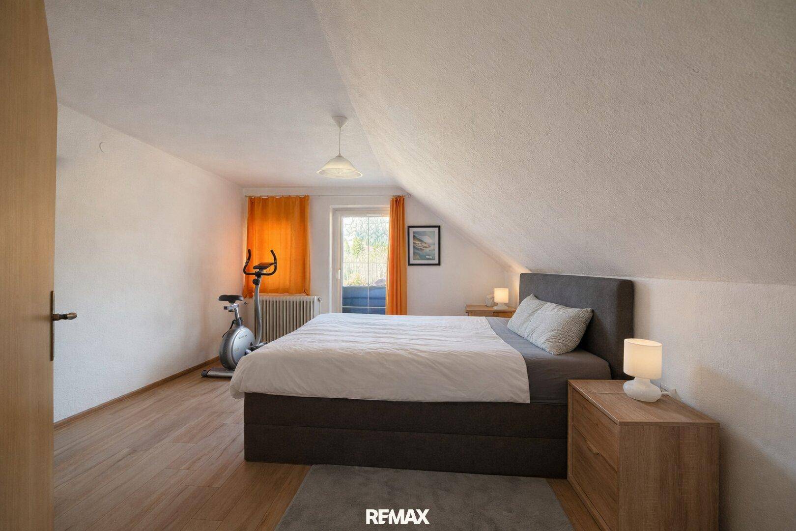 Helles Schlafzimmer im Dachgeschoss mit Holzboden, Sportgerät und Balkonzugang.
