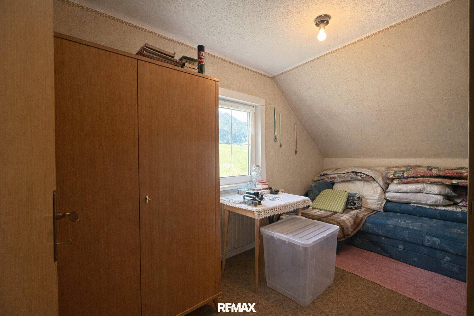 Kleines Zimmer im Dachgeschoss mit Schrägen, Schrank und Fenster mit Blick ins Grüne.