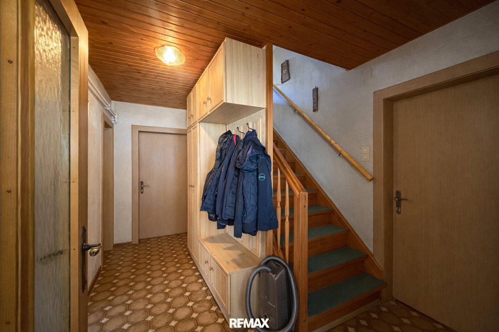 Eingangsbereich mit Holzvertäfelung an der Decke, Garderobe und Treppe zum Obergeschoss.