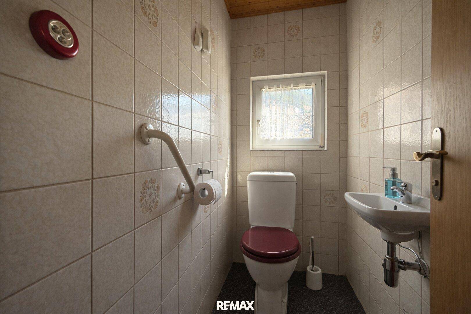 Separate Gästetoilette mit Fenster, Waschbecken und Haltegriffen für Barrierefreiheit.
