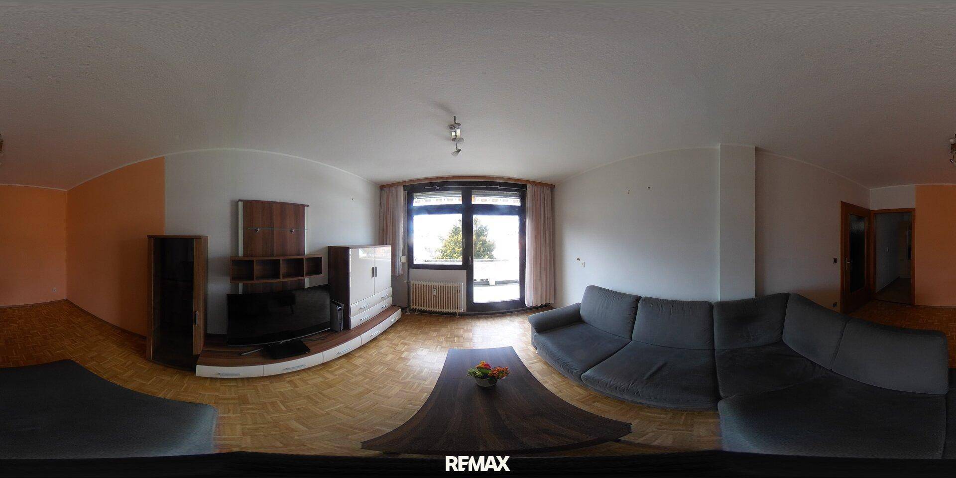 Geräumiges Wohnzimmer mit Parkettboden, großer Couch und Zugang zu einem Balkon.