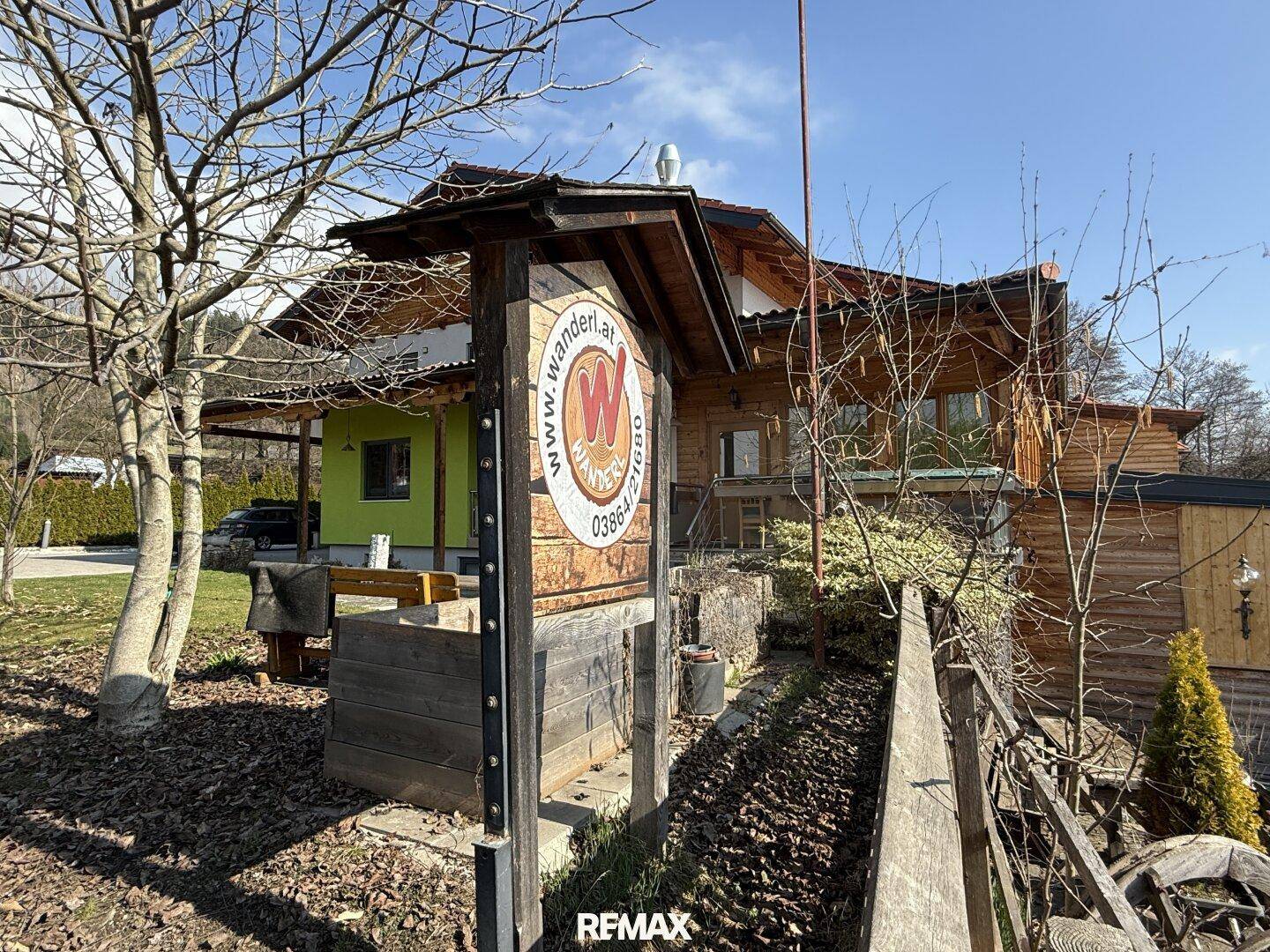 Außenansicht eines traditionellen Holzgebäudes mit einem Wegweiser und Bäumen im Vordergrund.