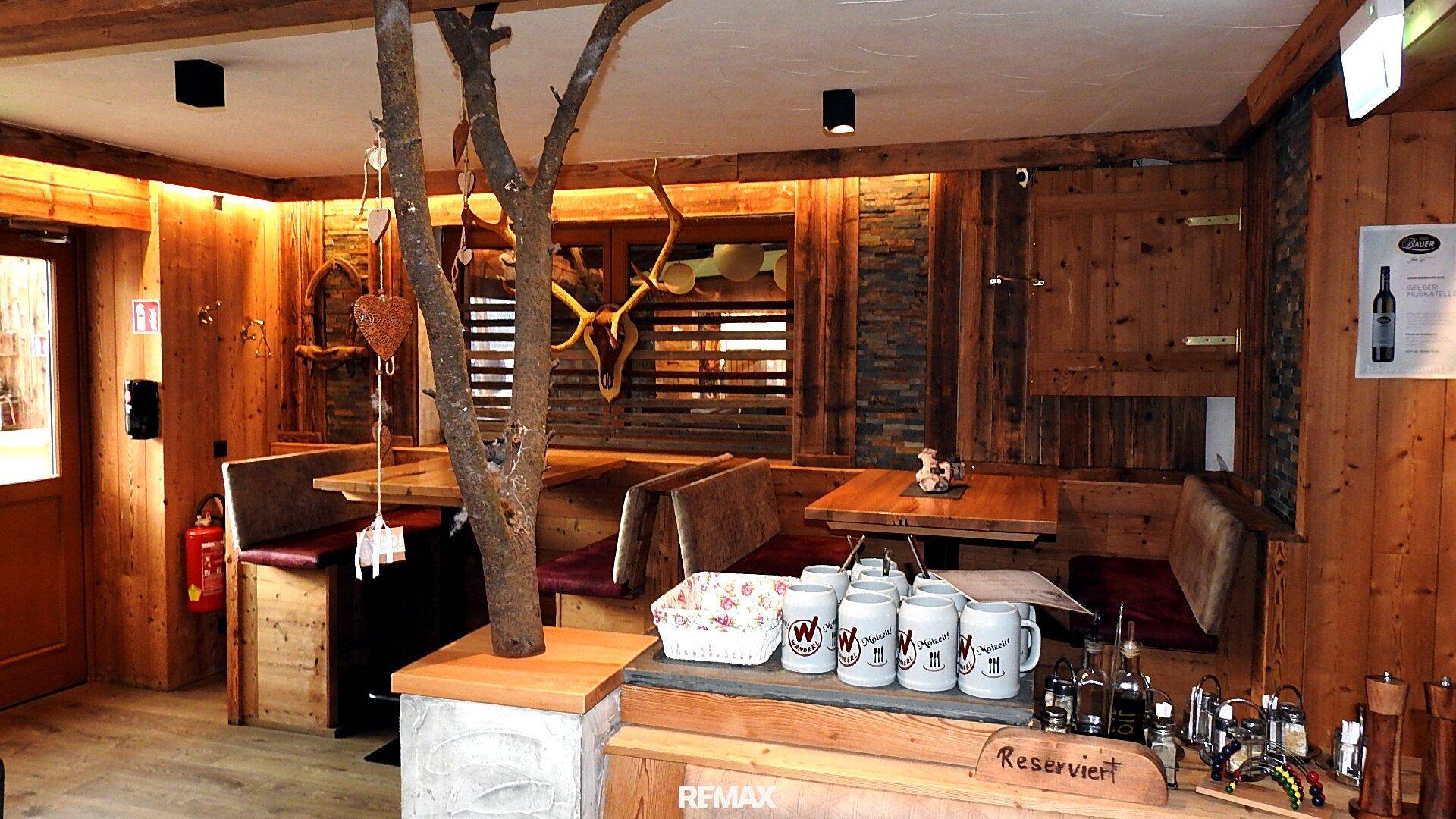 Gemütlicher Restaurantbereich im alpinen Stil mit Holztäfelung, Eckbänken und Hirschgeweih-Dekoration.