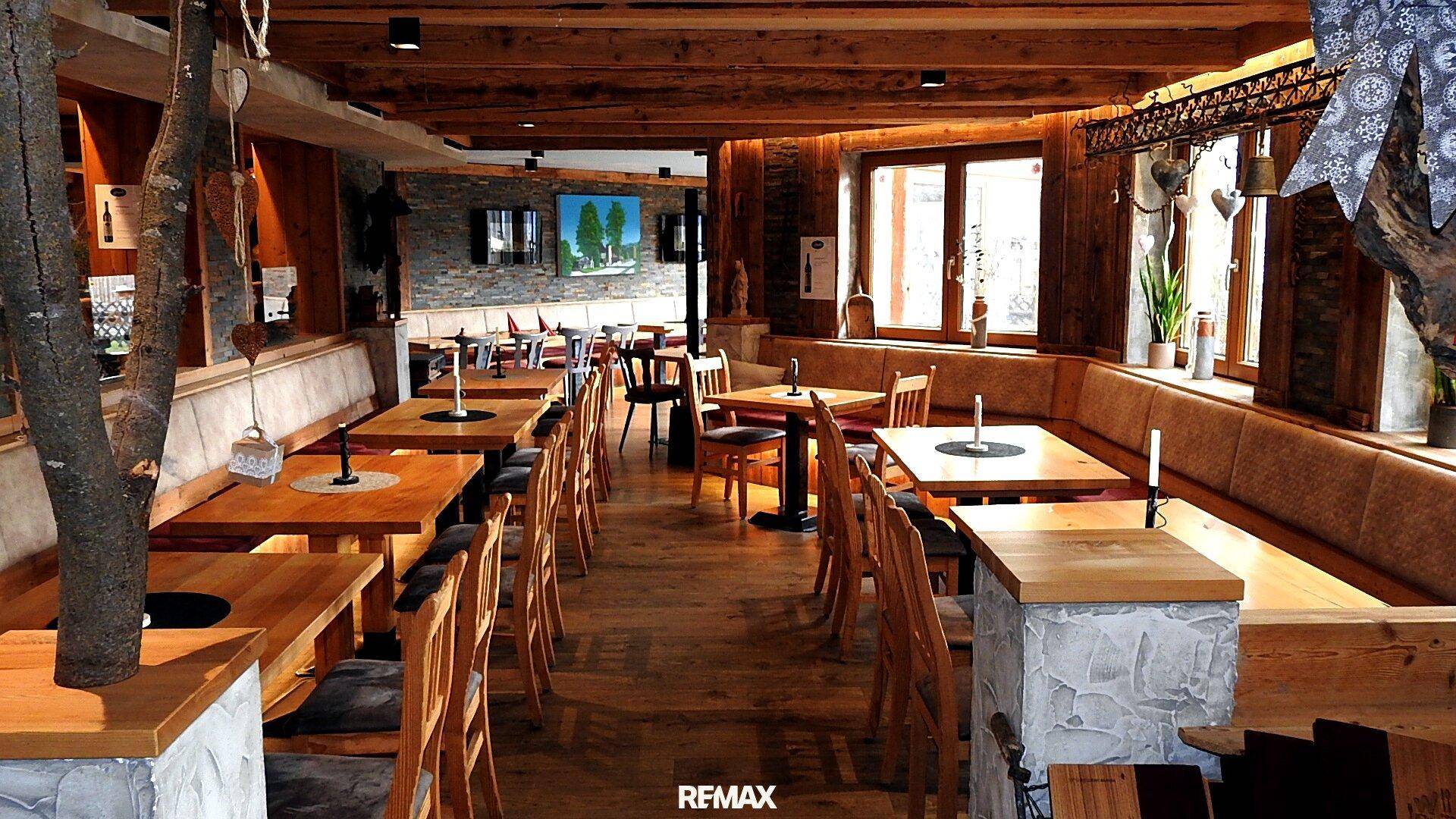 Geräumiger Restaurantbereich mit Holztischen, Bänken und Stühlen, durch große Fenster hell beleuchtet.