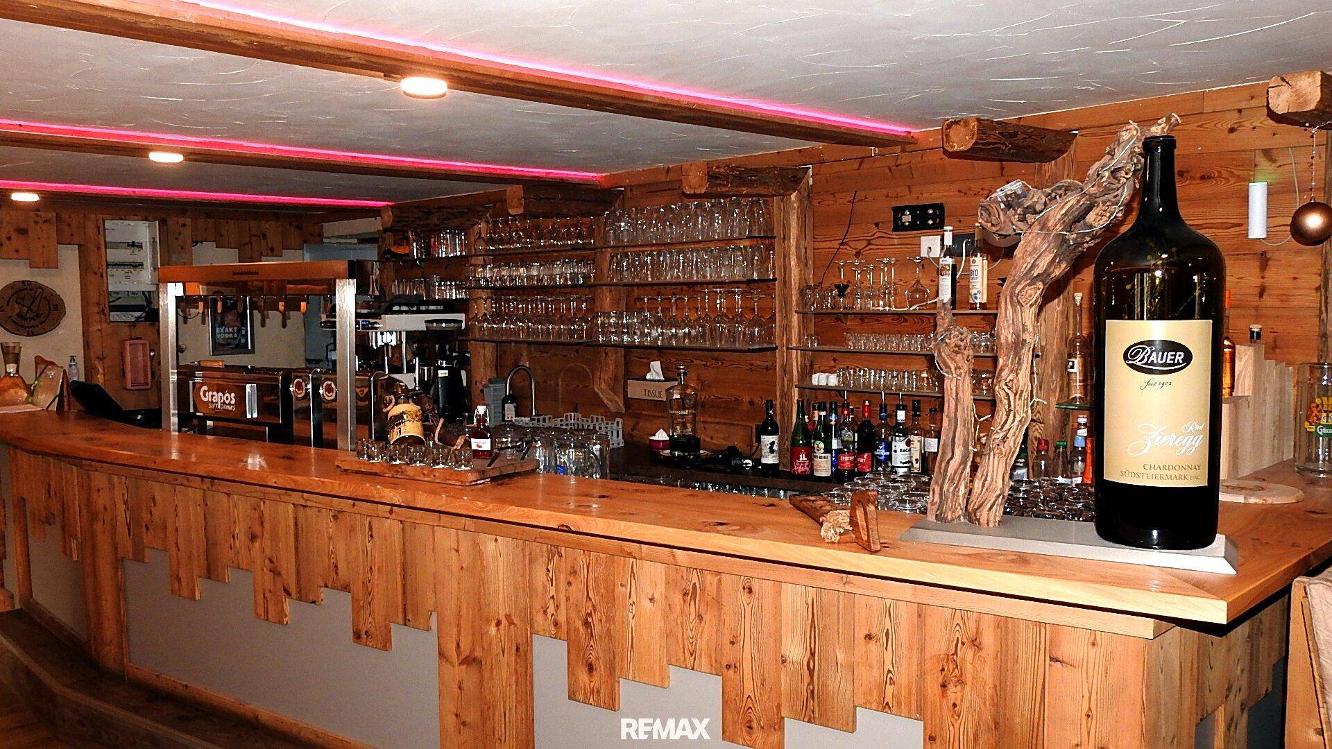 Lange Holztheke mit Zapfanlage, Gläserregalen und einer großen Weinflasche als Dekoration.
