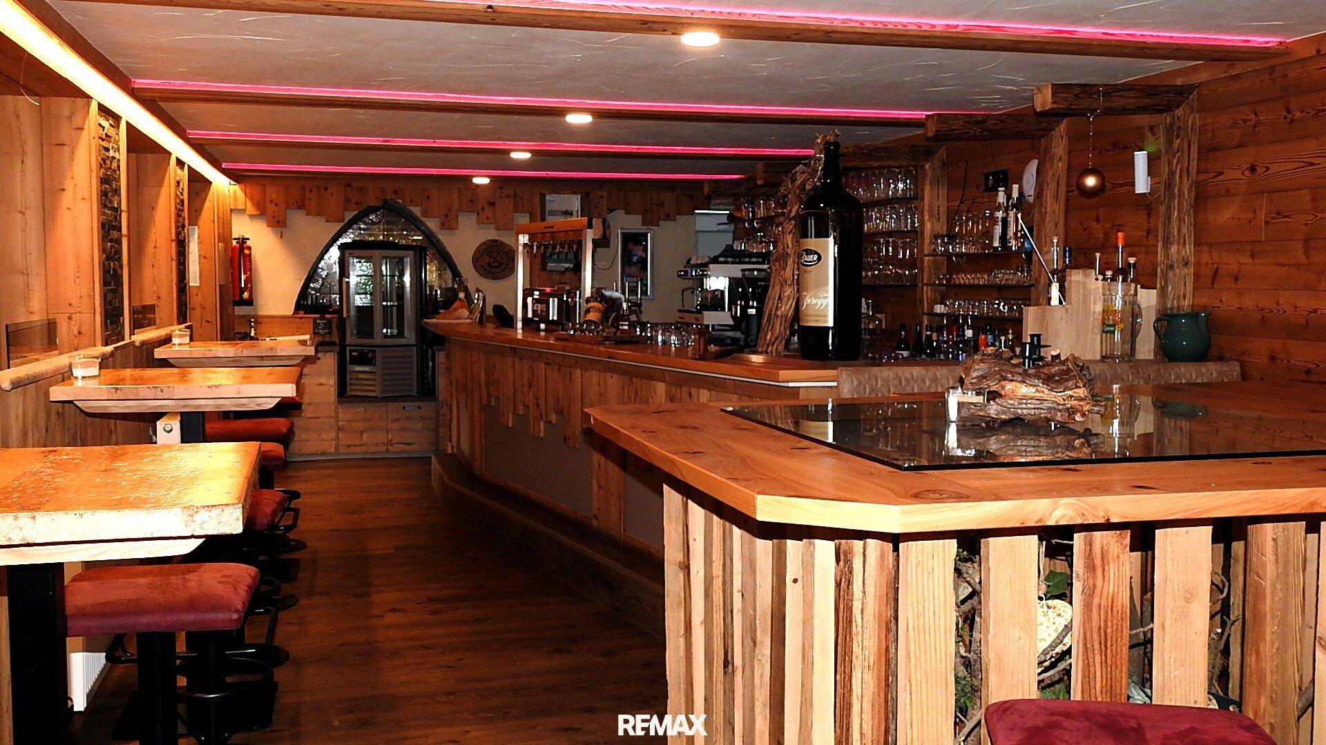 Bar- und Loungebereich mit Holzeinrichtung, gepolsterten Hockern und indirekter Deckenbeleuchtung.