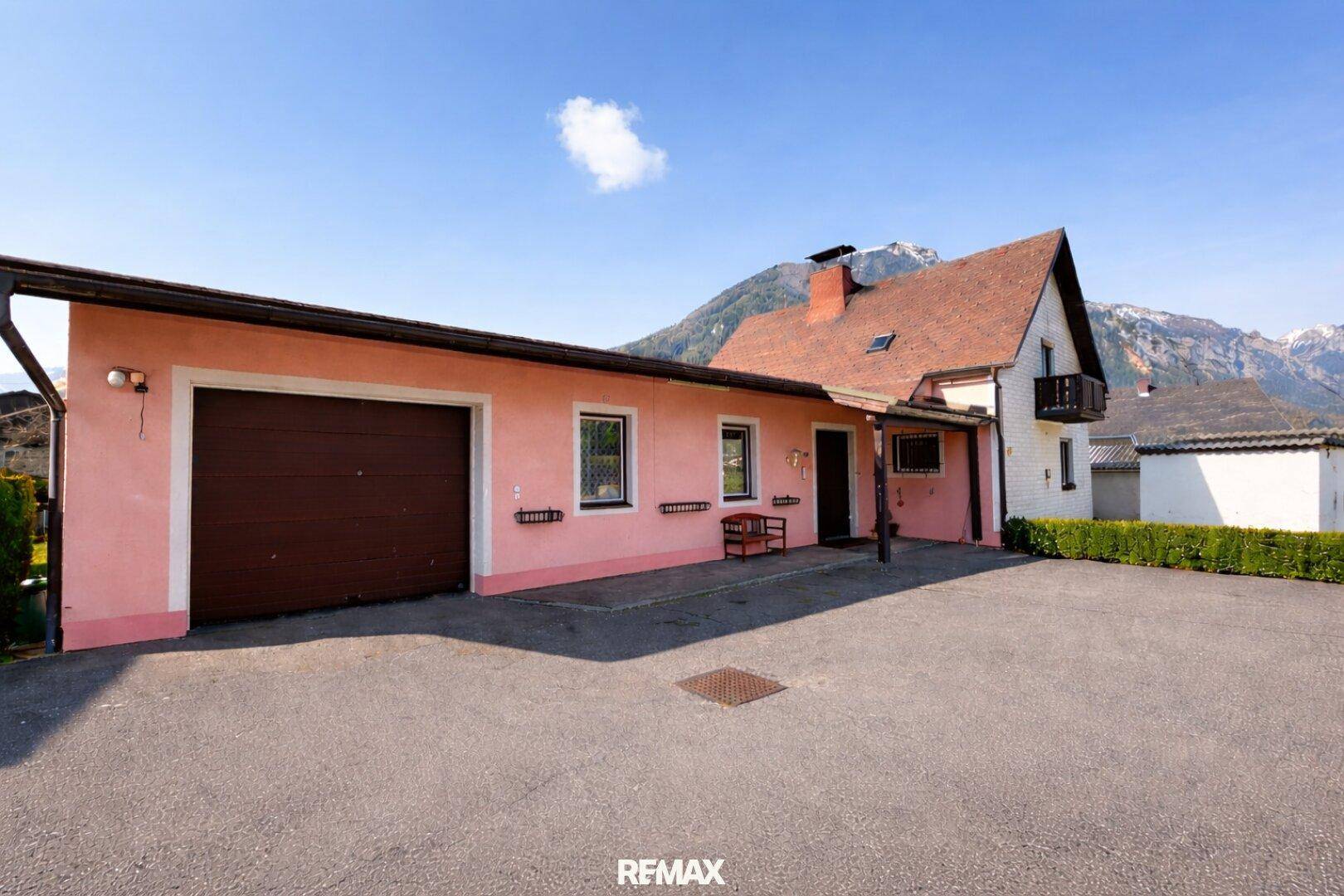 Ansicht des Hauses mit Garage und großem Vorplatz, umgeben von Bergen.
