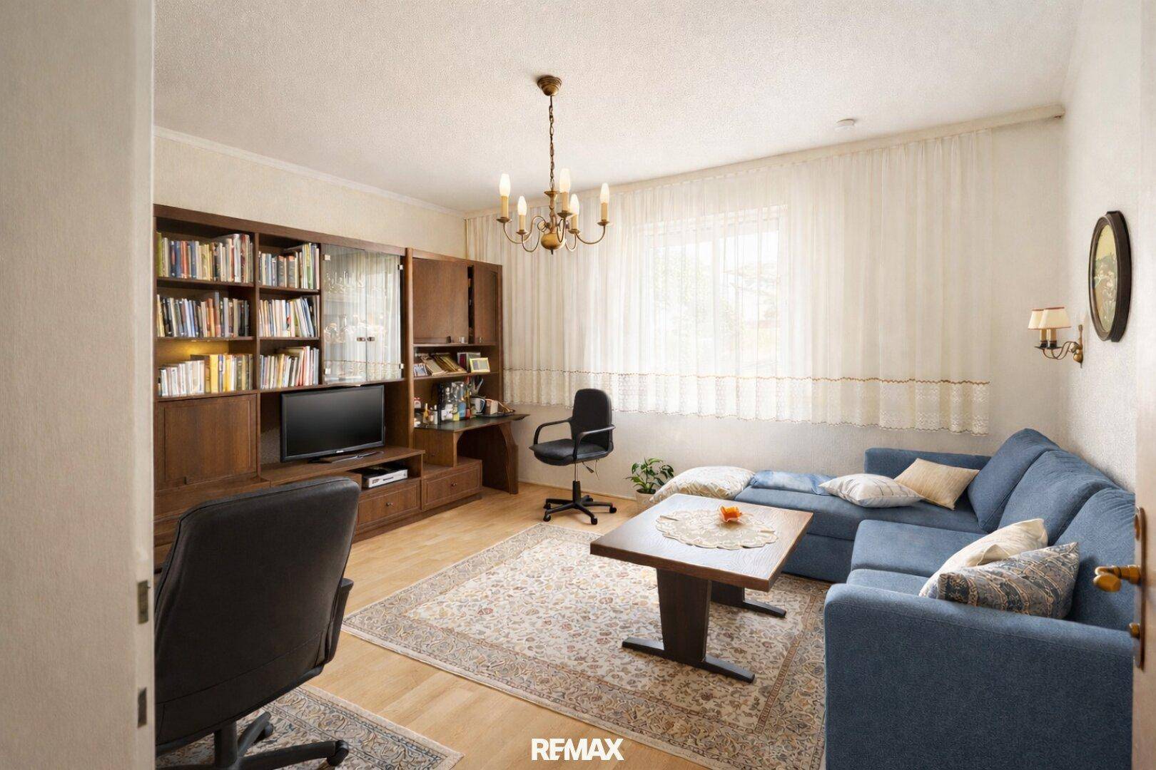 Gemütliches Wohnzimmer mit blauer Couch, Teppich und großem Fenster, hell und einladend.
