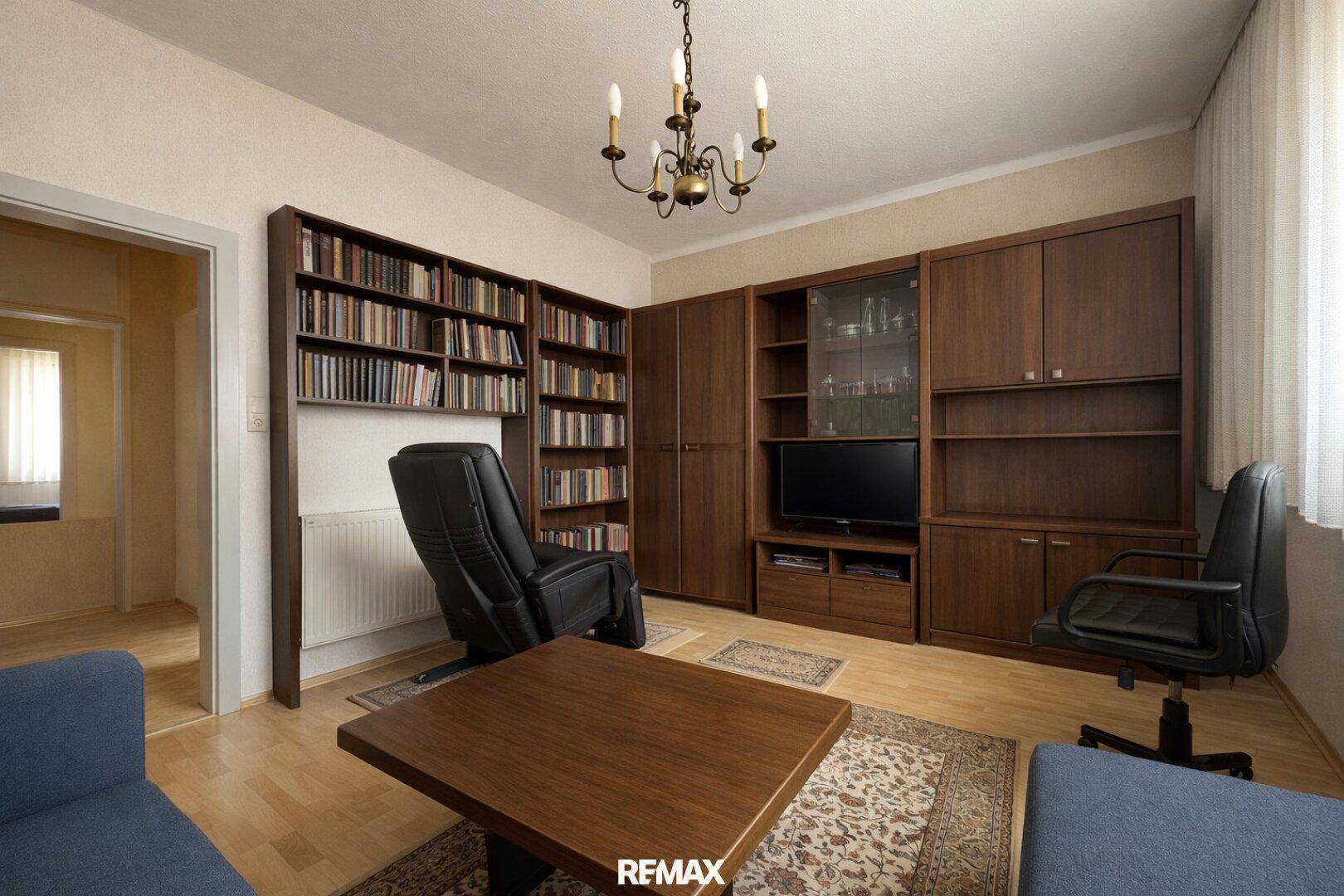 Wohnzimmer mit Bücherregal, Schreibtisch und Blick in den Flur, funktional eingerichtet.