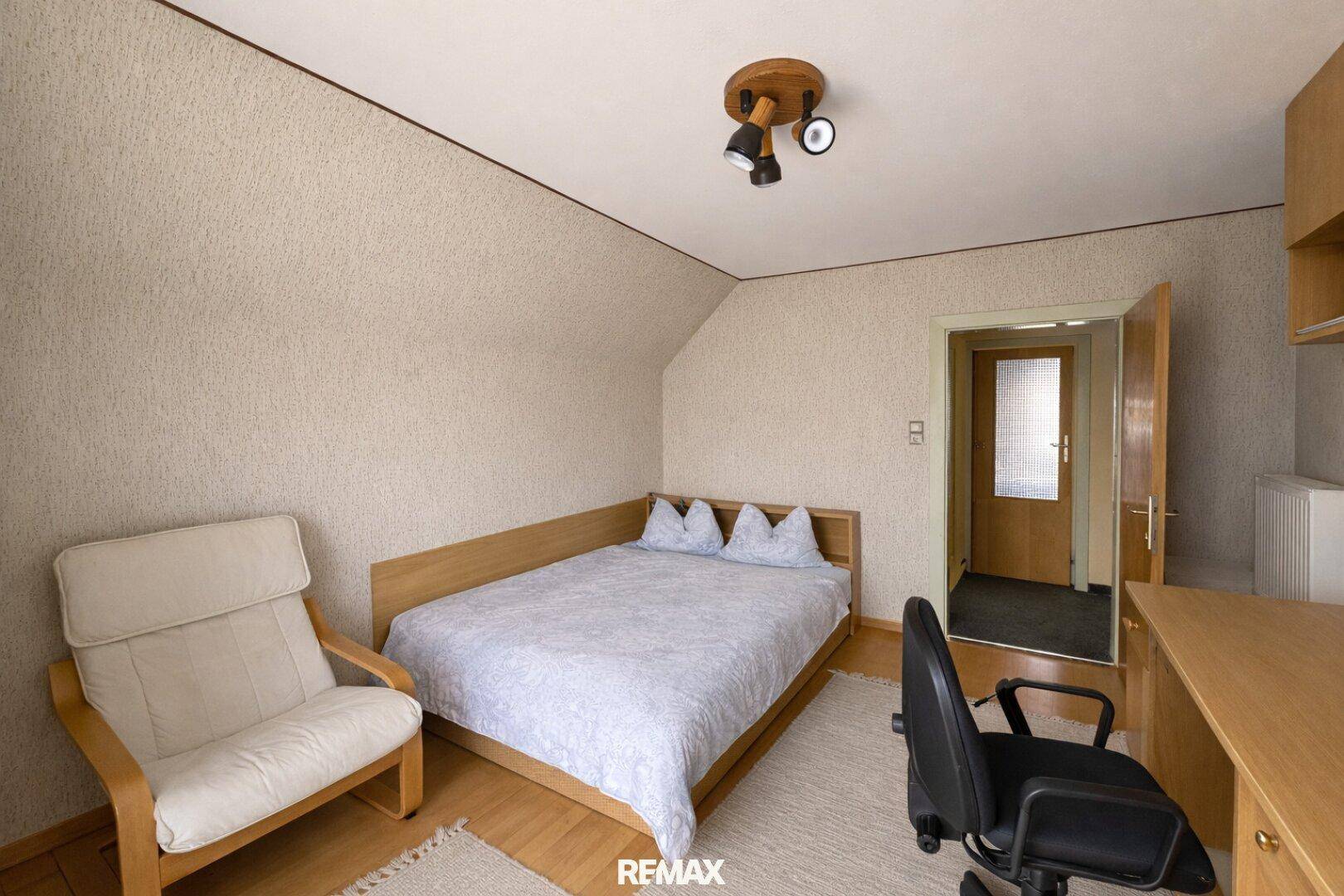 Schlafzimmer mit Doppelbett, Schreibtisch und Zugang zu einem weiteren Raum.