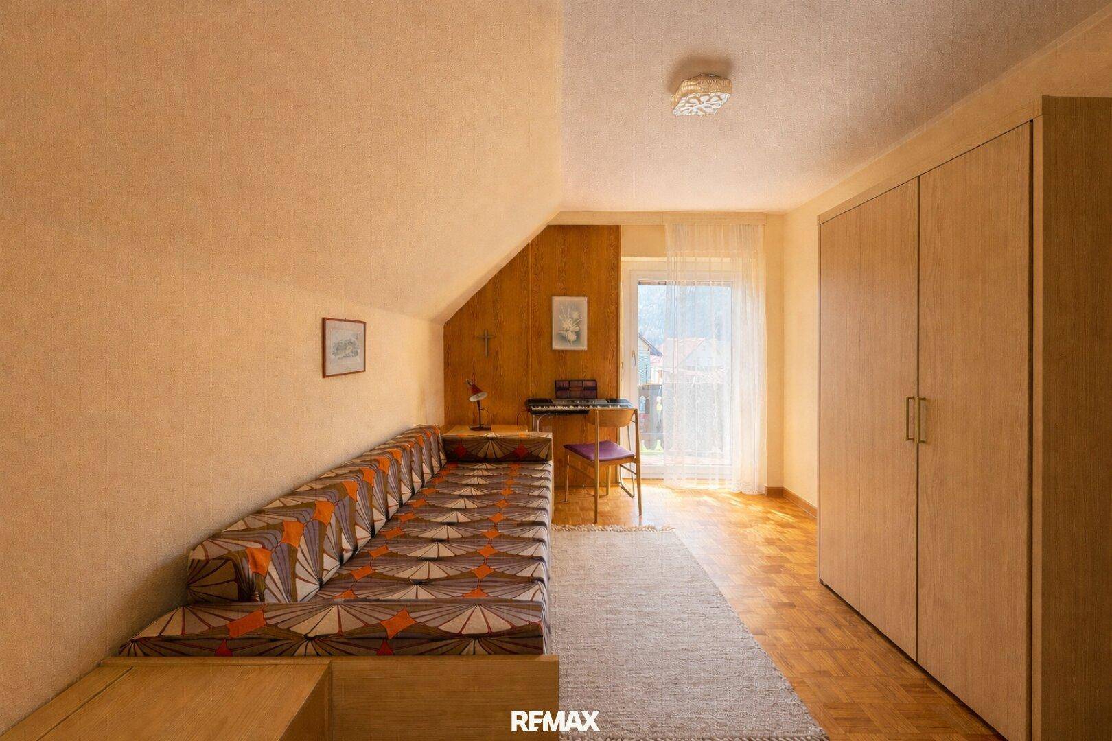 Gemütliches Schlafzimmer im Dachgeschoss mit Holzboden, Schlafcouch und Zugang zum Balkon.