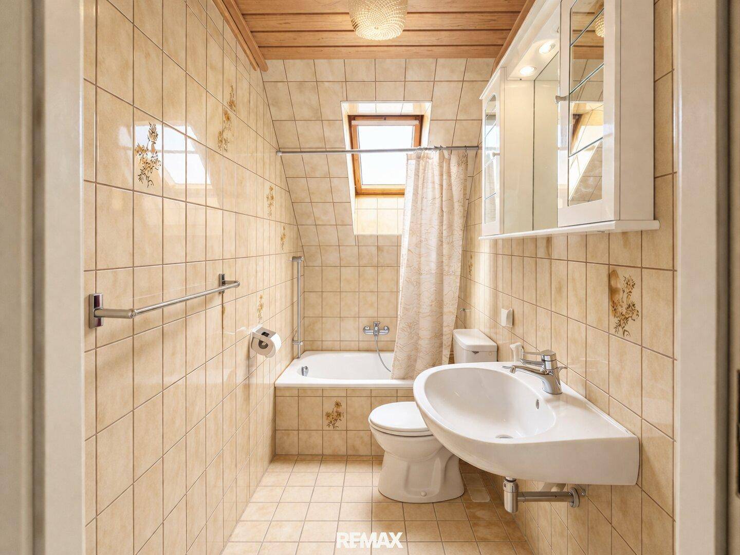 Gefliestes Badezimmer mit Badewanne, Waschbecken, WC und Dachfenster.