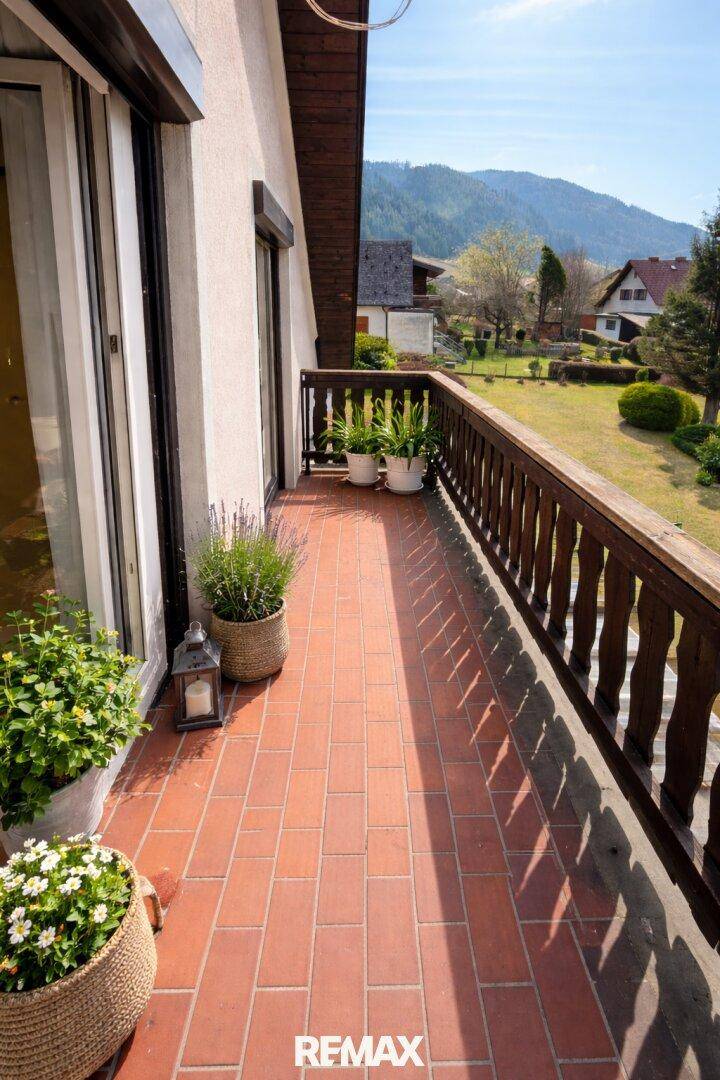 Sonniger Balkon mit Terrakottafliesen, Holzgeländer und Blick auf die Umgebung.