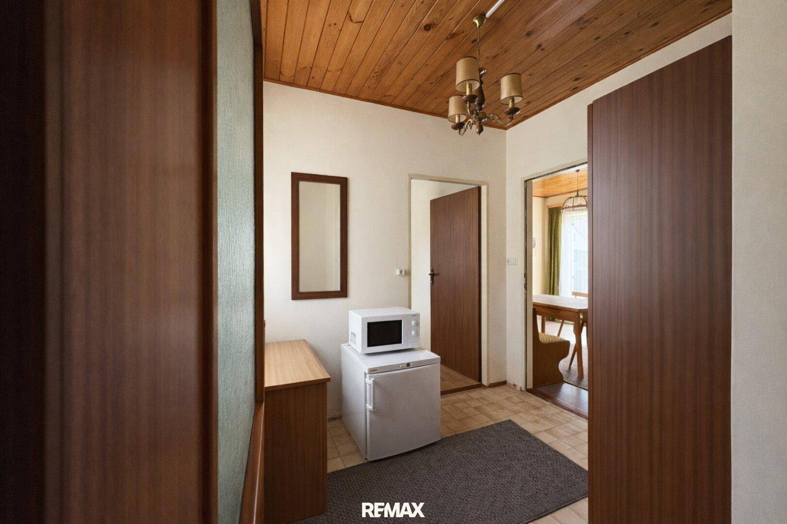 Flur mit Holzdecke, Mikrowelle und Kühlschrank, führt zu weiteren Räumen.