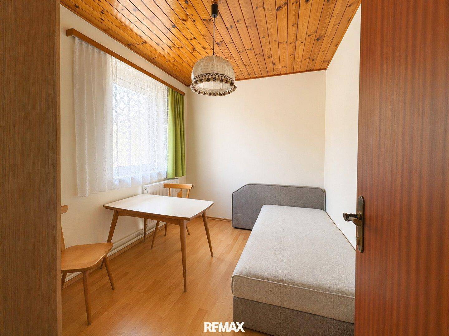 Helles Schlafzimmer mit Holzboden, Einzelbett und Fenster mit Vorhängen.