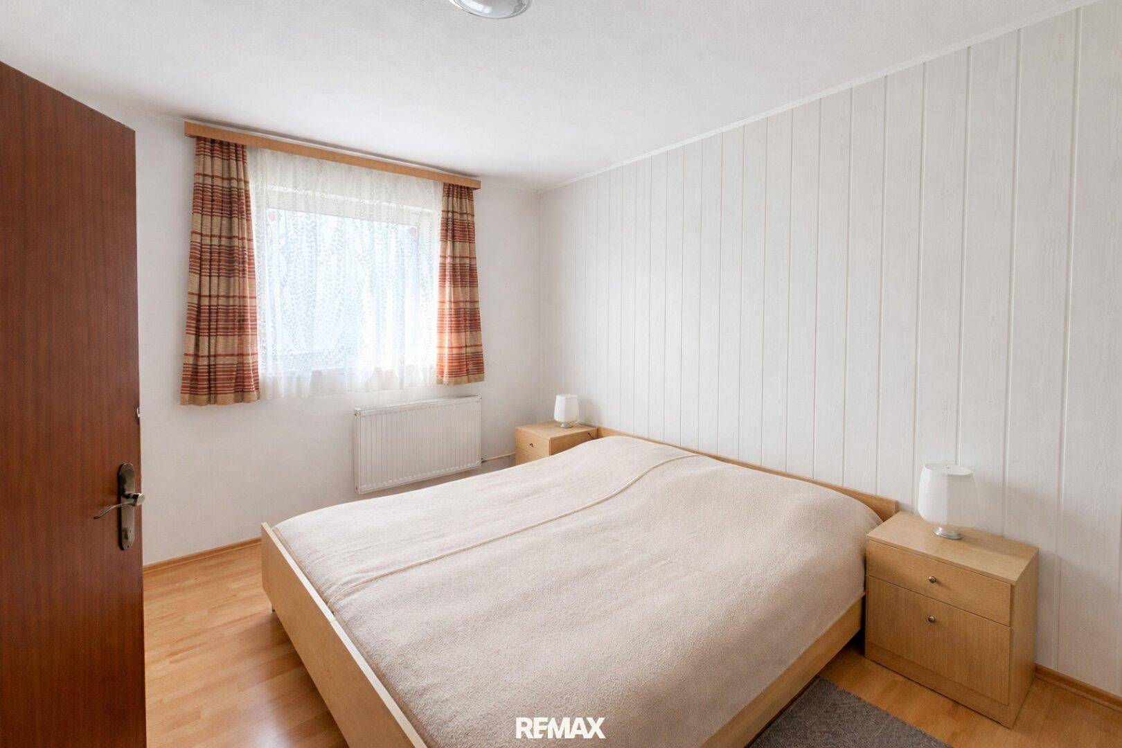 Geräumiges Schlafzimmer mit Doppelbett, Holzboden und Fenster mit Blick nach draußen.