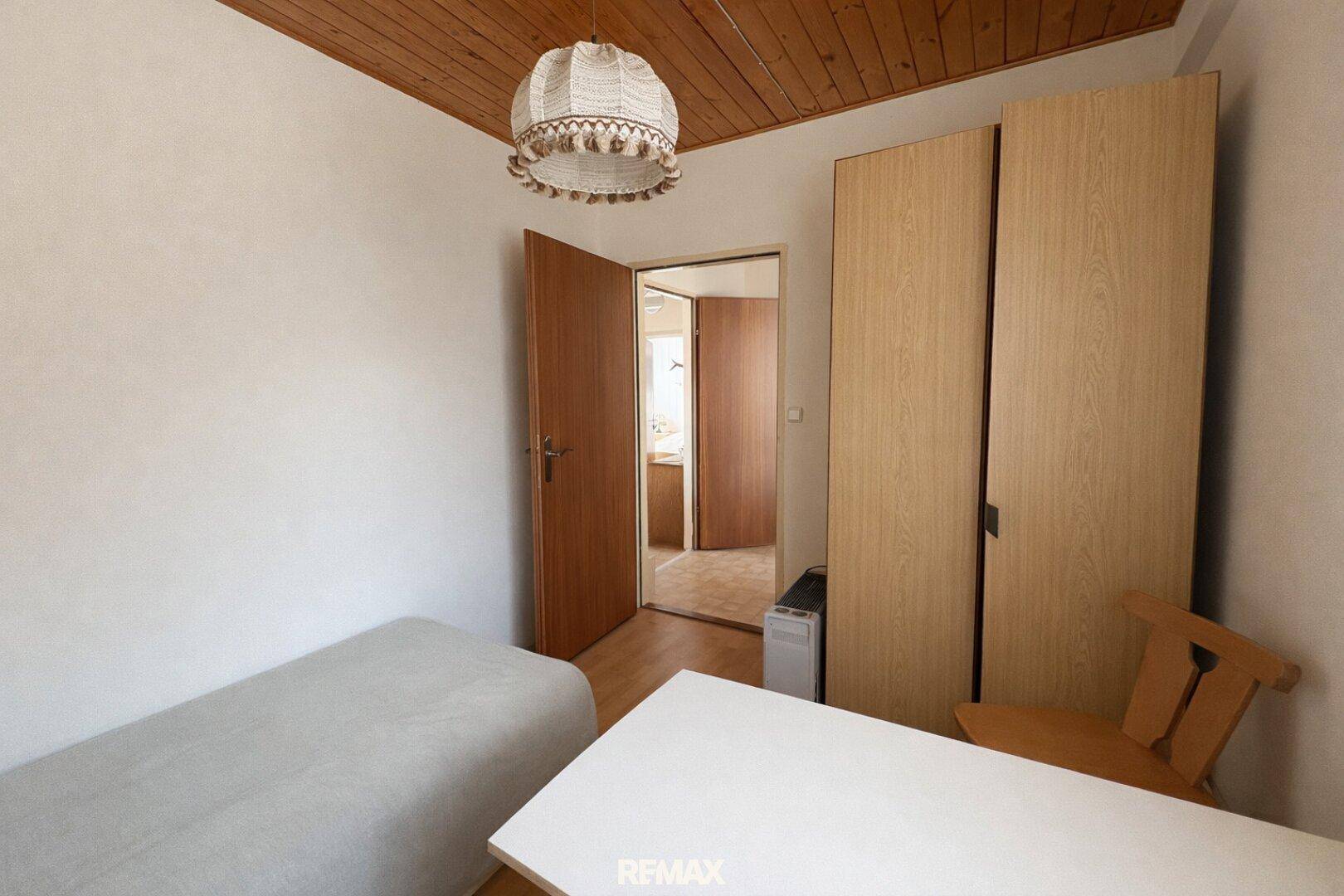 Schlafzimmer mit Holzboden, Tisch und Kleiderschränken, führt zu einem Flur.
