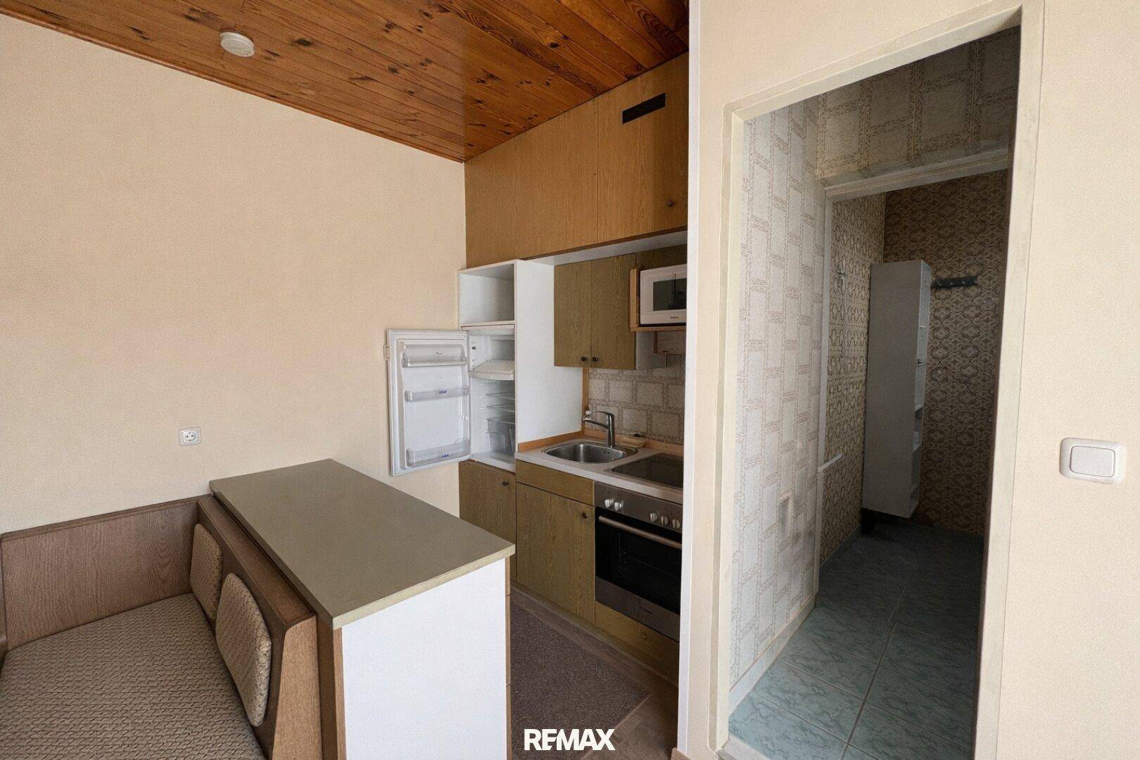 Kleine Küchenzeile mit Kühlschrank, Spüle und Sitzgelegenheit, funktional und kompakt.