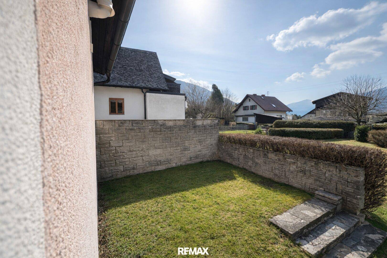 Kleiner Gartenbereich mit Rasenfläche und Steinmauer, sonnig und gepflegt.