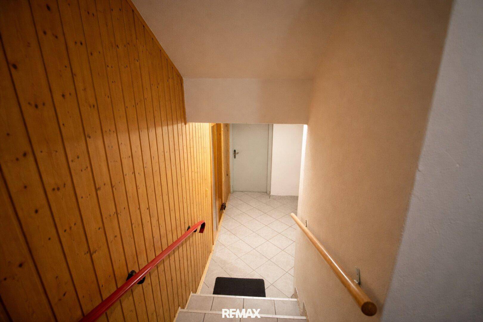 Treppenhaus mit Holzvertäfelung und gefliestem Boden, das zu weiteren Räumen führt.