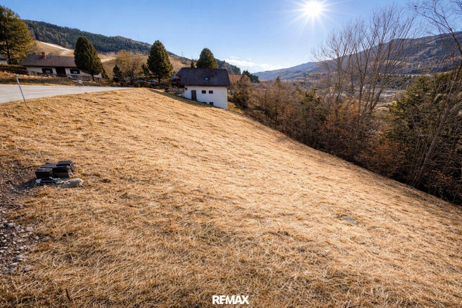 Sonniges Hanglage-Grundstück mit Blick auf die umliegende Berglandschaft und ein kleines Haus.