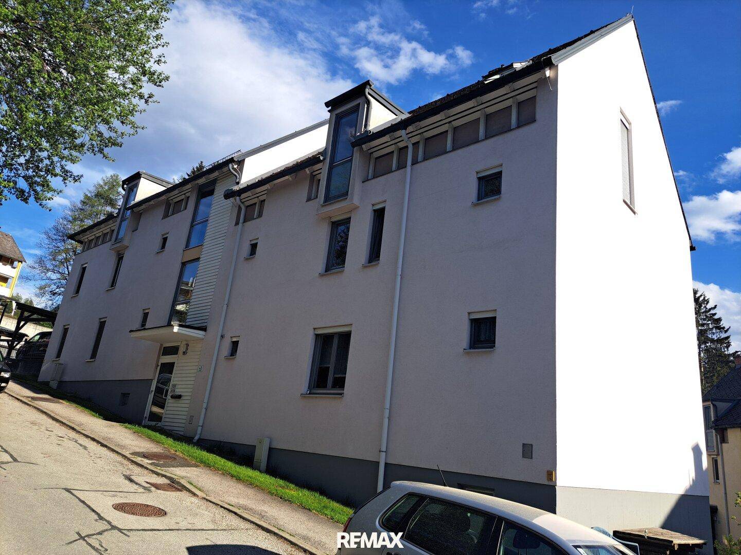 Moderne Gebäudefassade mit großen Fenstern und Satteldach unter blauem Himmel.