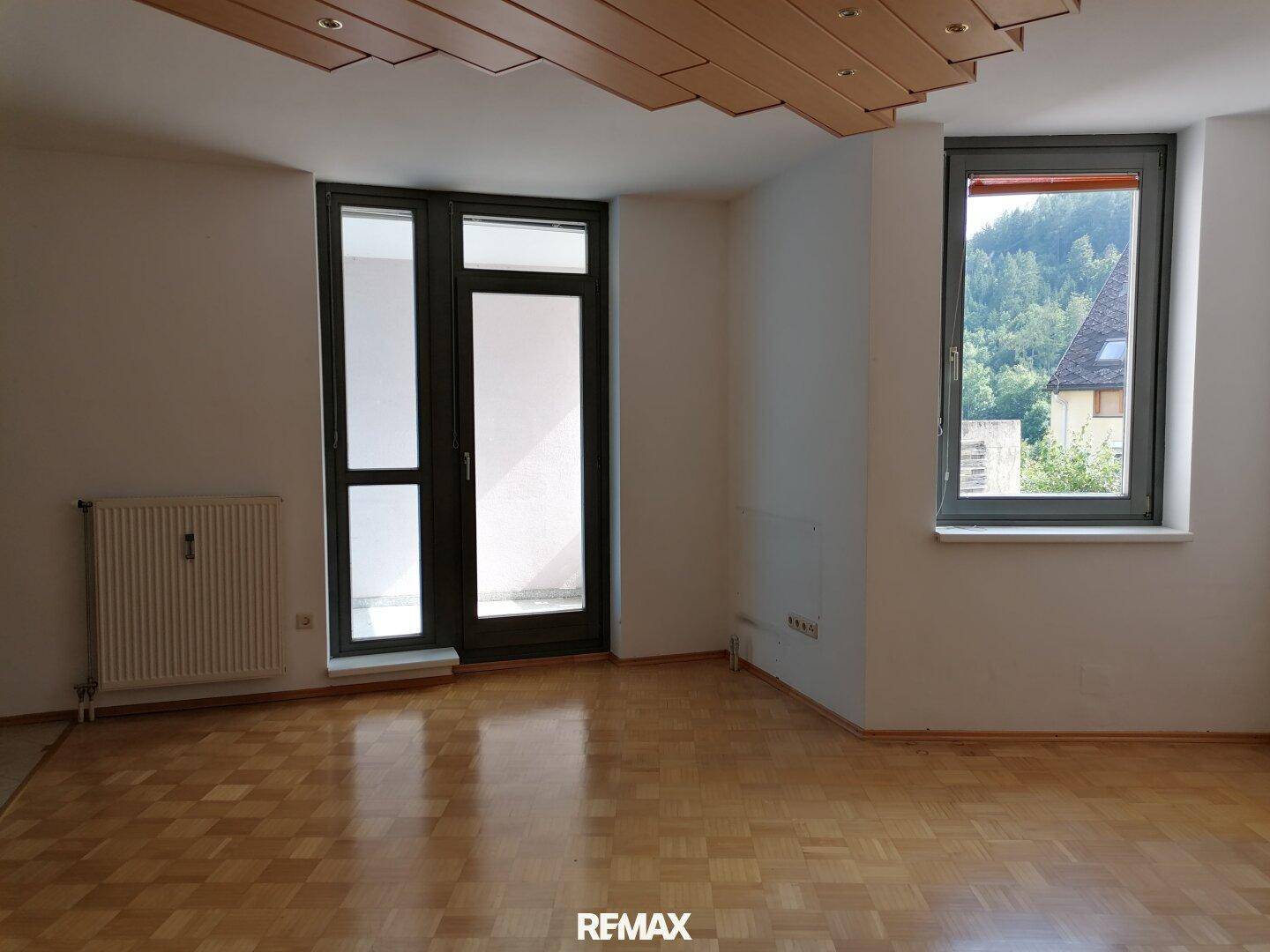 Helles Wohnzimmer mit Parkettboden, großen Fenstern und Blick ins Grüne.