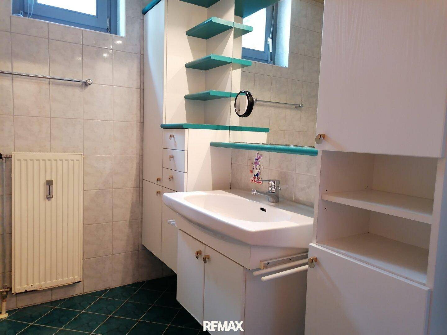 Badezimmer mit Waschbecken, Spiegelschrank, Regalen und einem Fenster für Tageslicht.