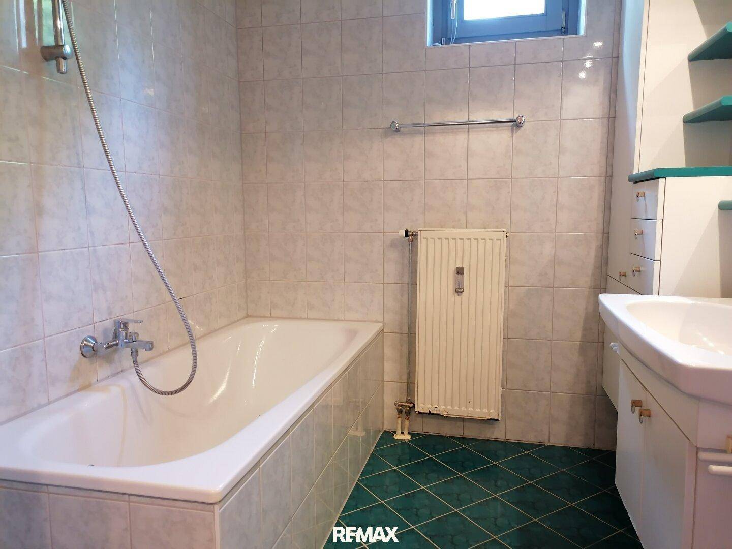 Badezimmer mit Badewanne, Duscharmatur und gefliesten Wänden und Boden.