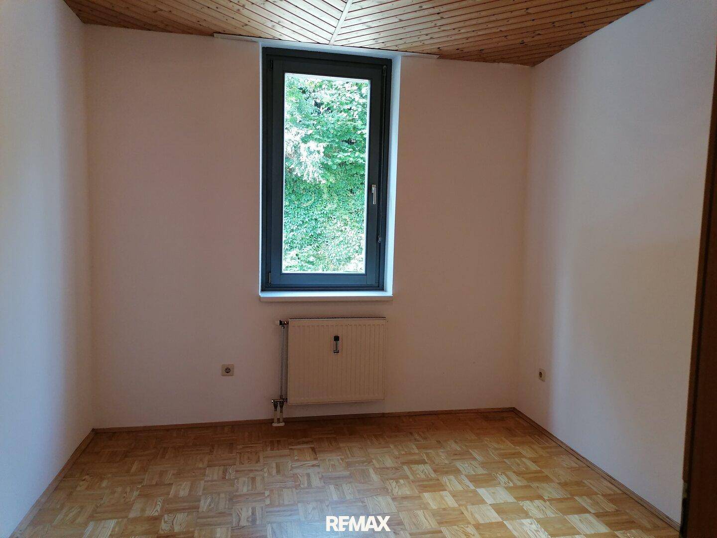 Helles Zimmer mit Parkettboden, weiß gestrichenen Wänden und Blick ins Grüne.