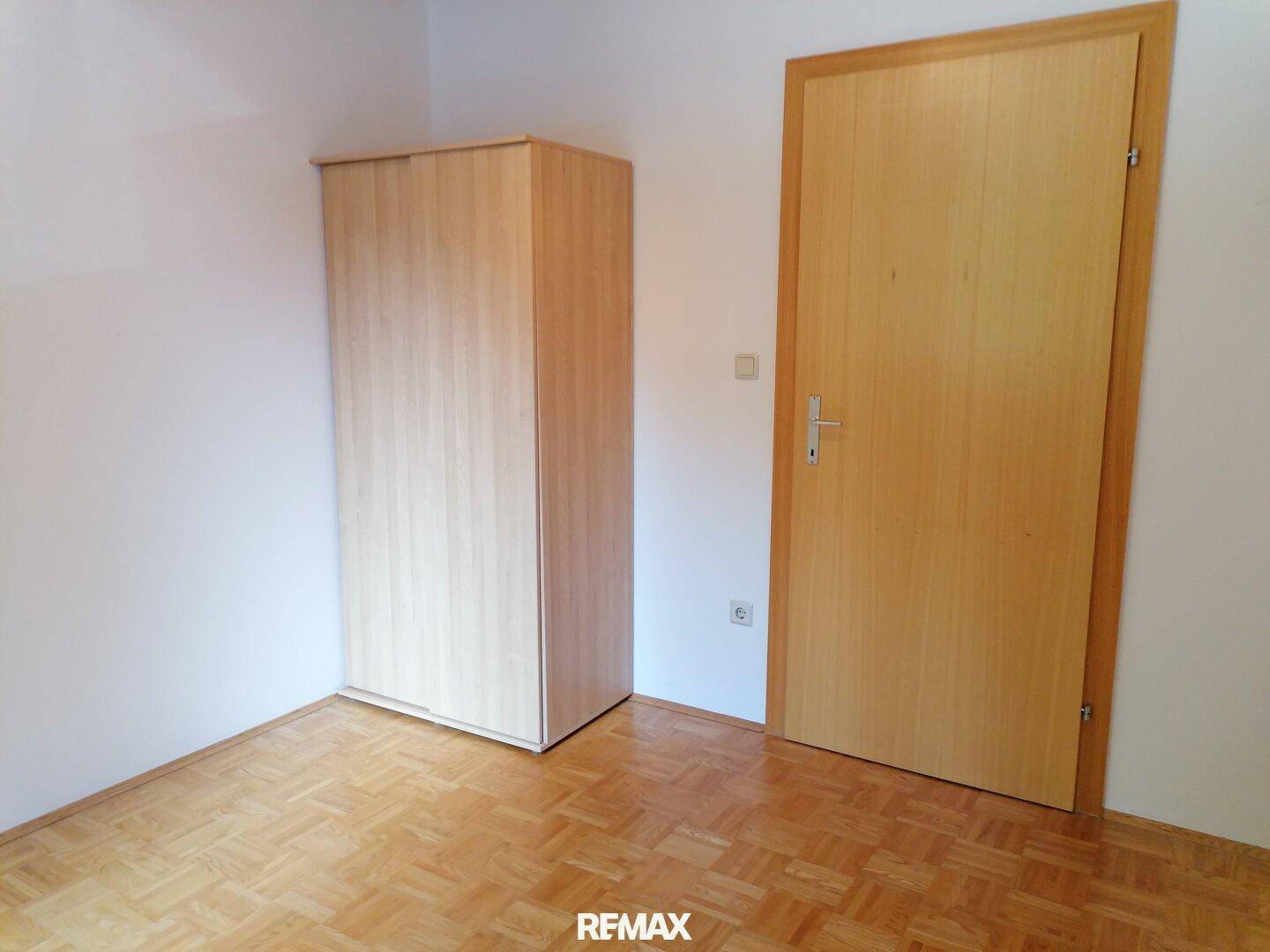 Zimmer mit Parkettboden, einem Kleiderschrank aus Holz und einer Holztür.