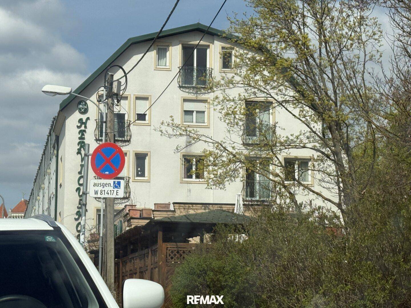 Seitenansicht des Gebäudes mit Balkonen und umliegender Vegetation, teilweise verdeckt.