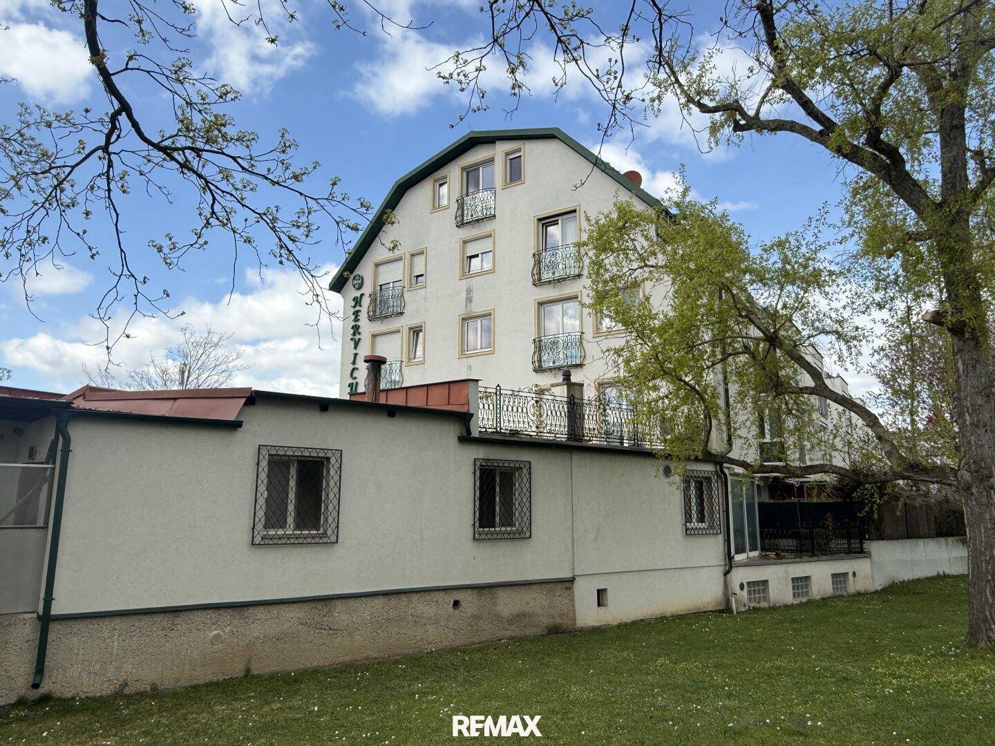 Rückansicht des Gebäudes mit Rasenfläche und Bäumen unter blauem Himmel.