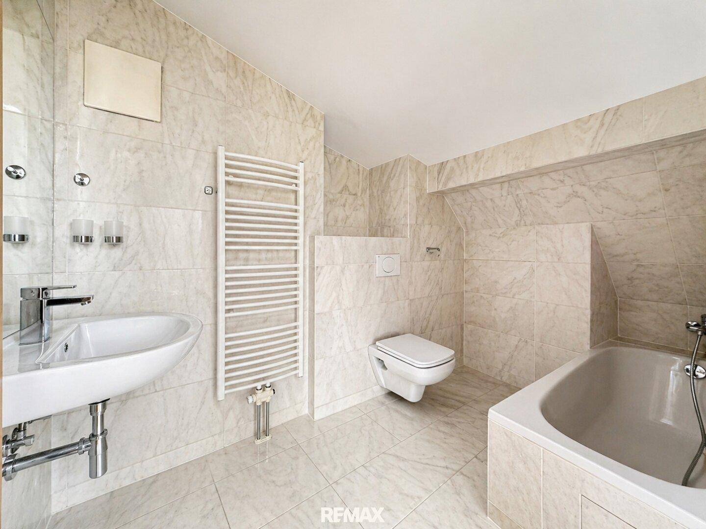 Helles Badezimmer mit beigefarbenen Fliesen, Badewanne, WC und beheiztem Handtuchhalter.