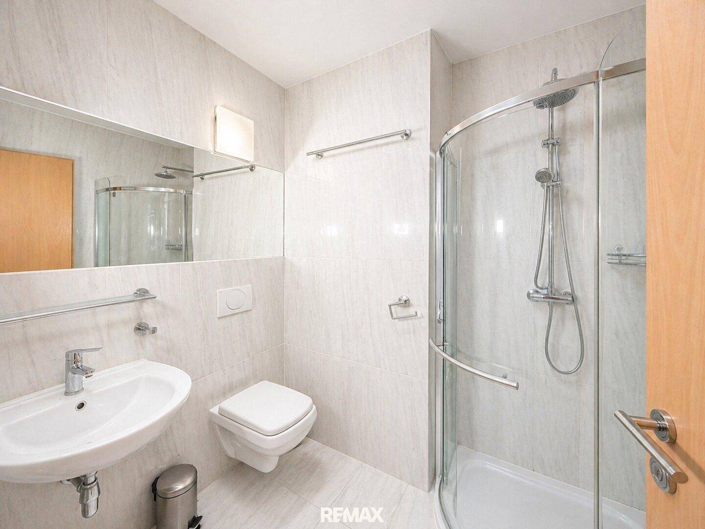 Modernes Badezimmer mit Duschkabine, Wand-WC und großem Spiegel über dem Waschbecken.