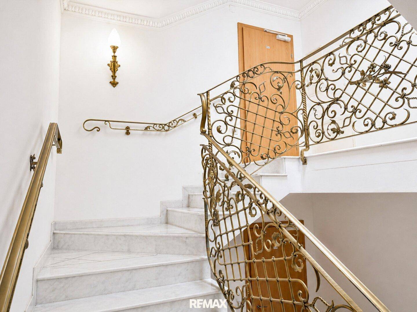 Elegantes Treppenhaus mit Marmorstufen und kunstvoll geschmiedetem Geländer in Goldtönen.