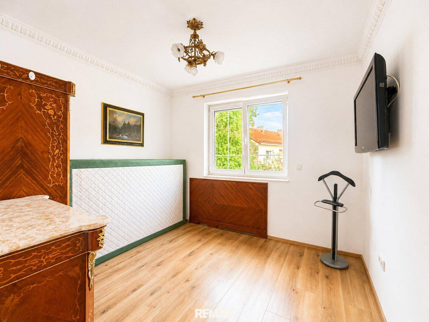 Helles Schlafzimmer mit Holzboden, Fenster und klassischem Mobiliar in warmen Holztönen.