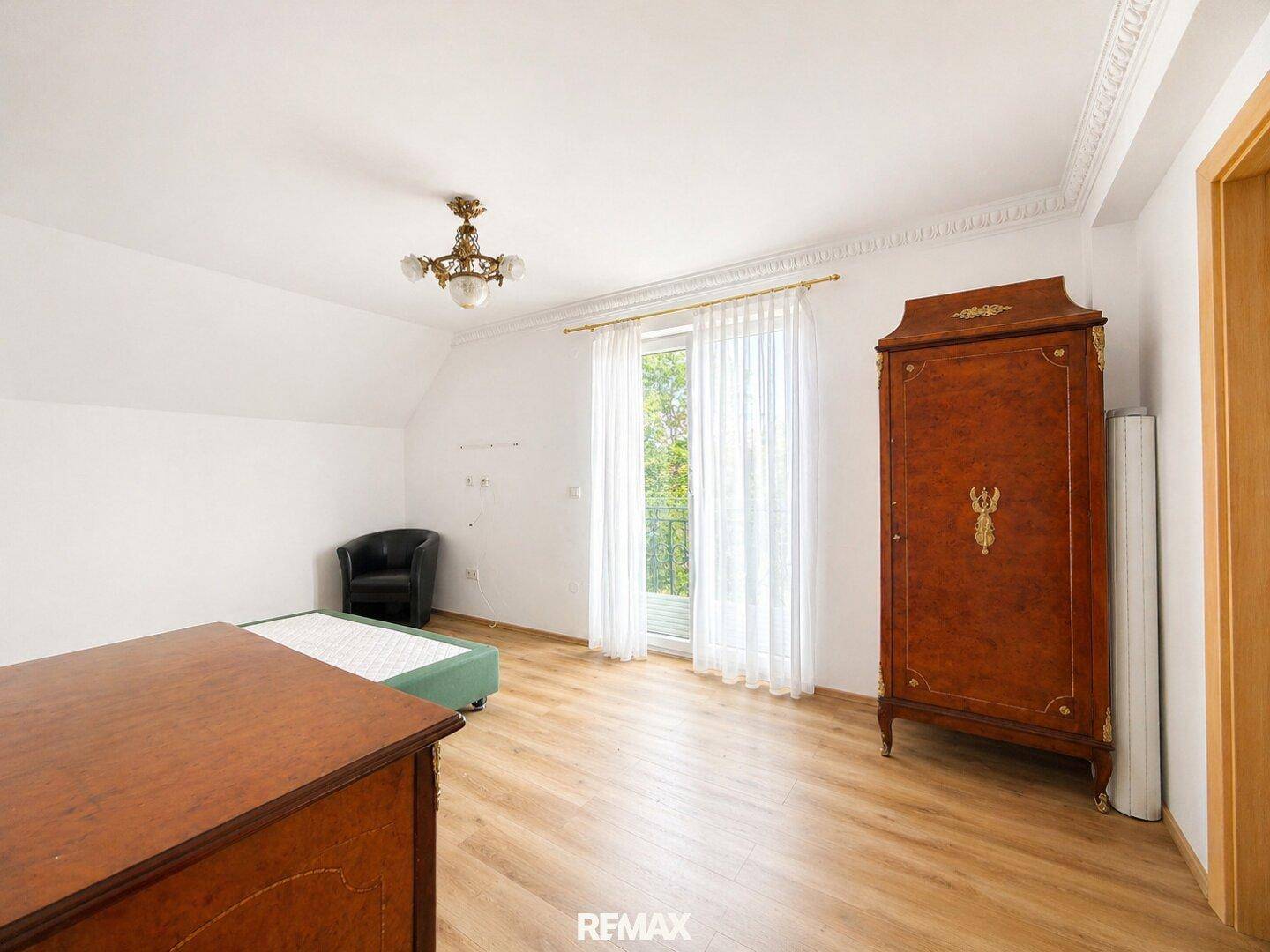 Helles Schlafzimmer mit Holzboden, Balkonzugang und klassischem Kleiderschrank.