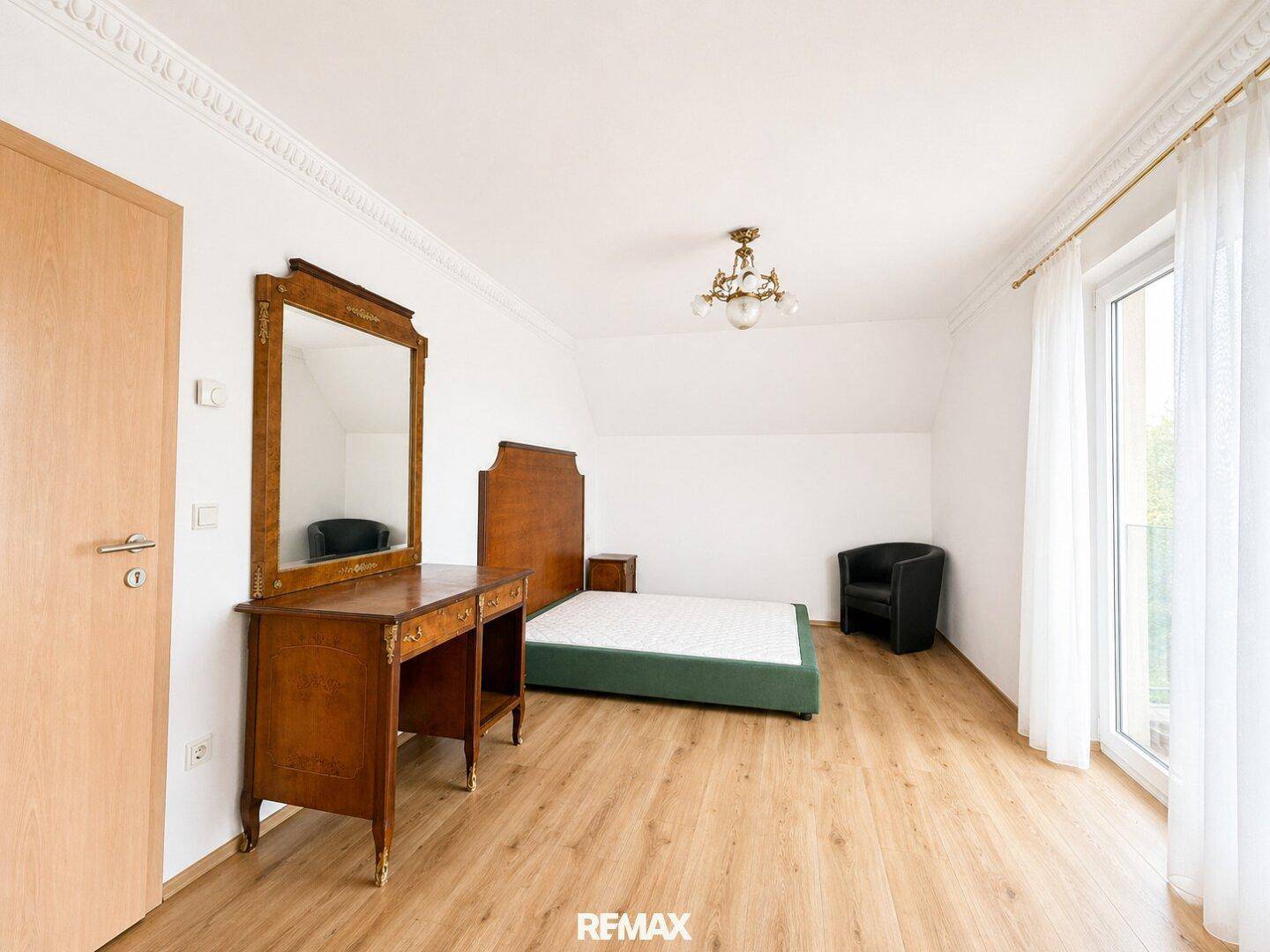 Schlafzimmer mit Holzboden, Schminktisch und Zugang zu einem französischen Balkon.