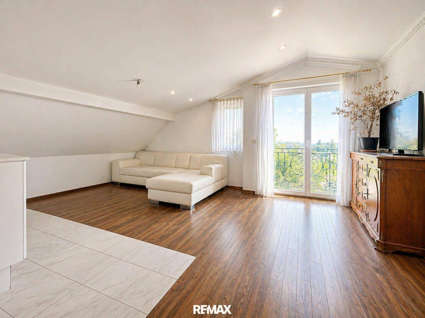 Heller Wohnbereich mit Holzboden, weißem Sofa und Blick ins Grüne durch große Fenster.
