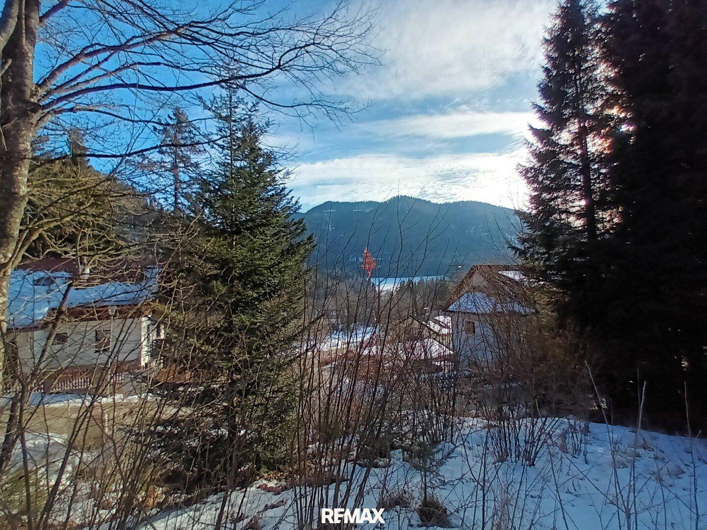 Sonniger Wintertag mit verschneiter Landschaft, Häusern und Bergen unter blauem Himmel.
