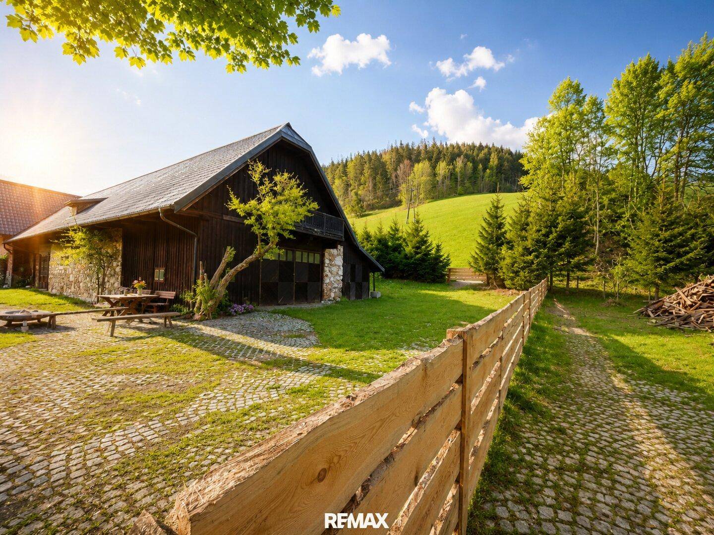 Rustikales Holzhaus mit Steinfassade und gepflastertem Hof in ländlicher Umgebung.