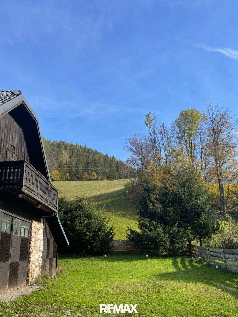 Ländliches Gebäude mit Holzbalkon und Blick auf bewaldete Hügel und Wiesen.