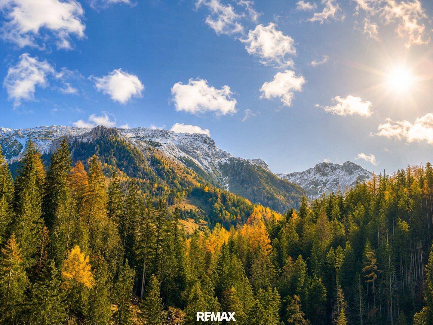 Beeindruckende Berglandschaft mit schneebedeckten Gipfeln und herbstlich gefärbten Wäldern.