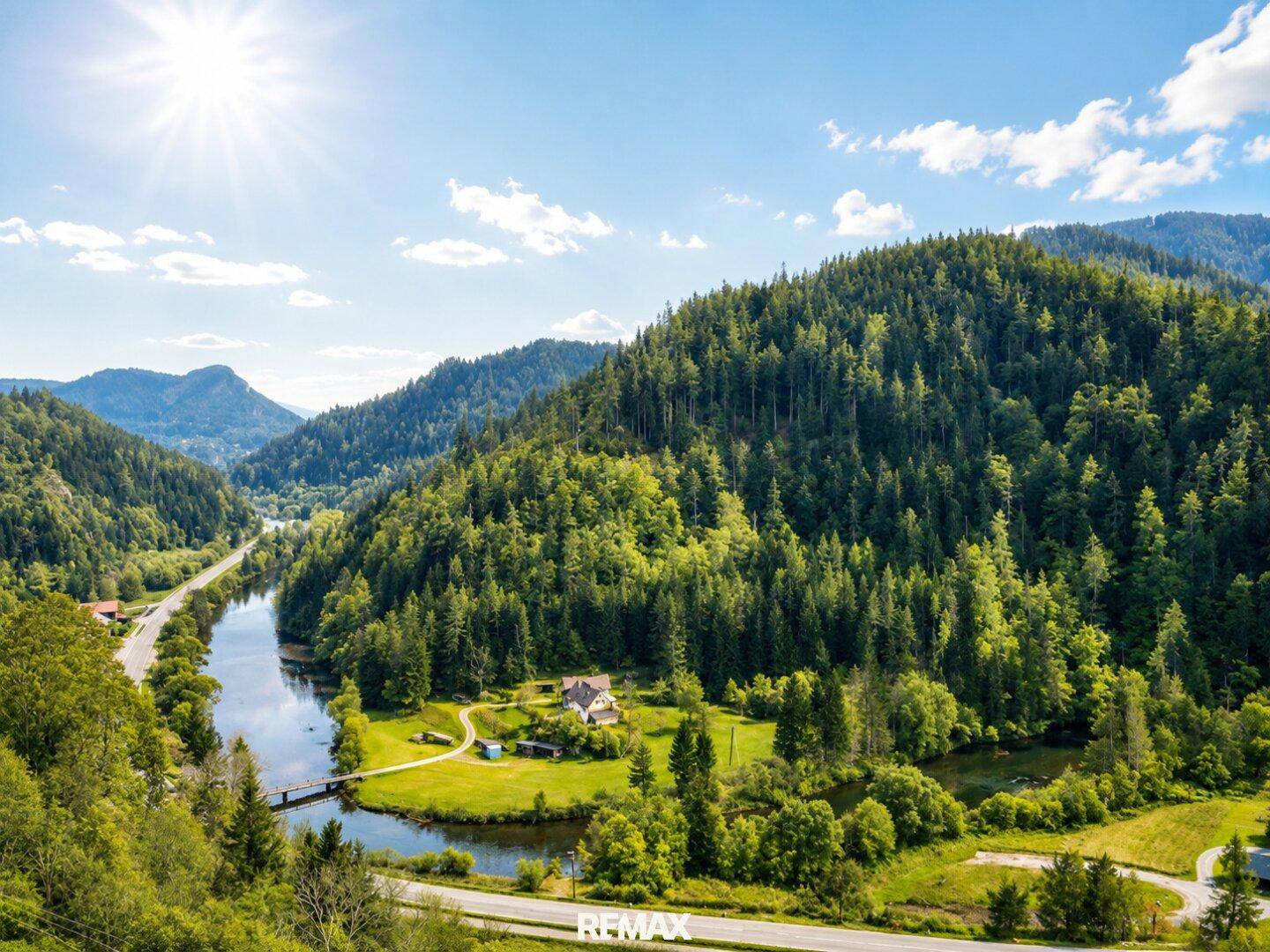 Malerische Luftaufnahme eines Flusstals mit bewaldeten Hügeln und vereinzelten Häusern.