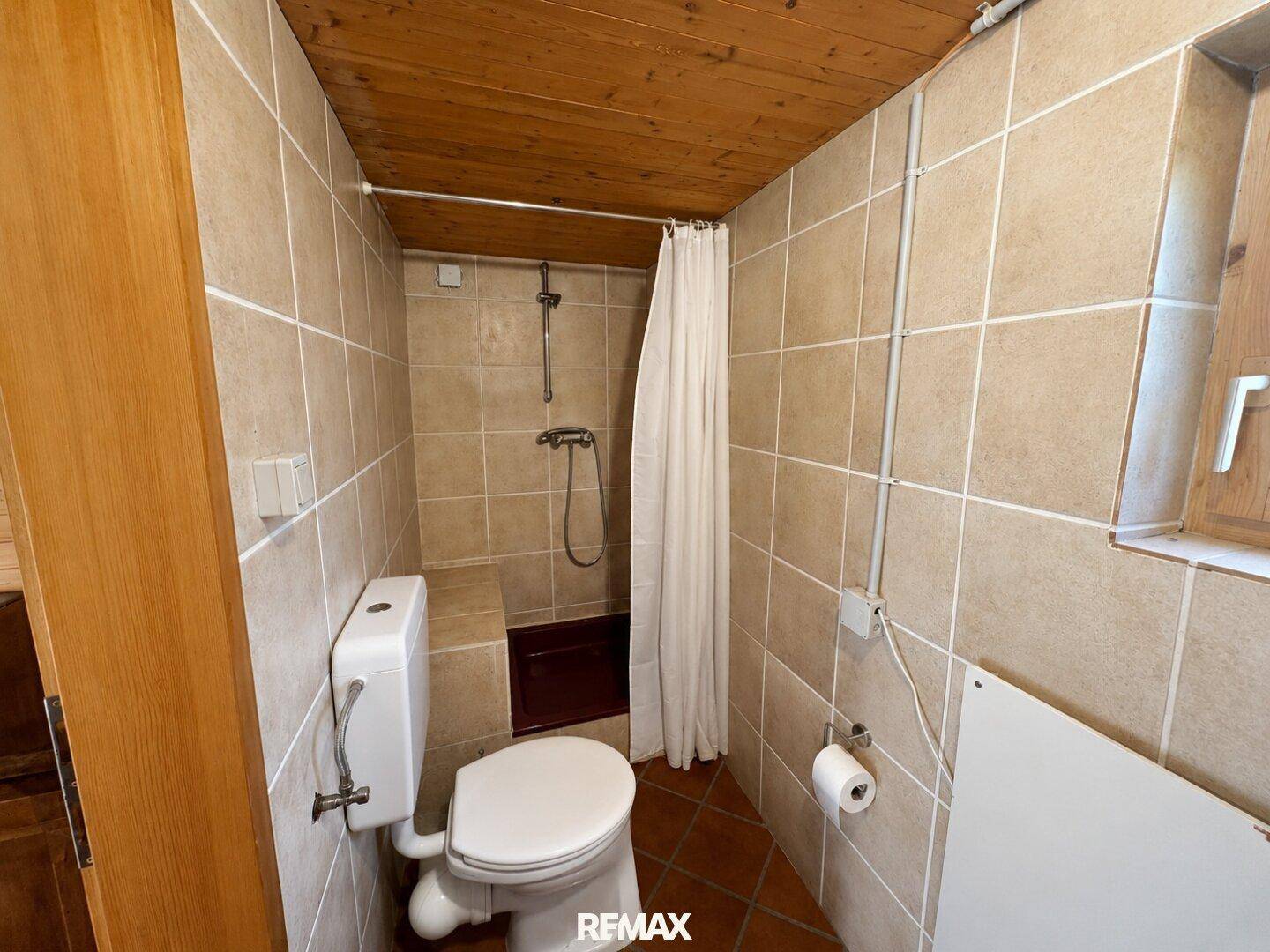 Badezimmer mit beigefarbenen Fliesen, Toilette und Duschbereich, einfach und sauber.