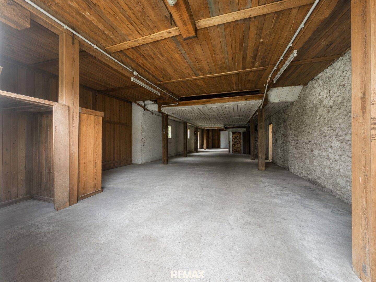 Großer, leerer Raum mit Holzbalken, Steinwänden und Betonboden, bereit für Ausbau.