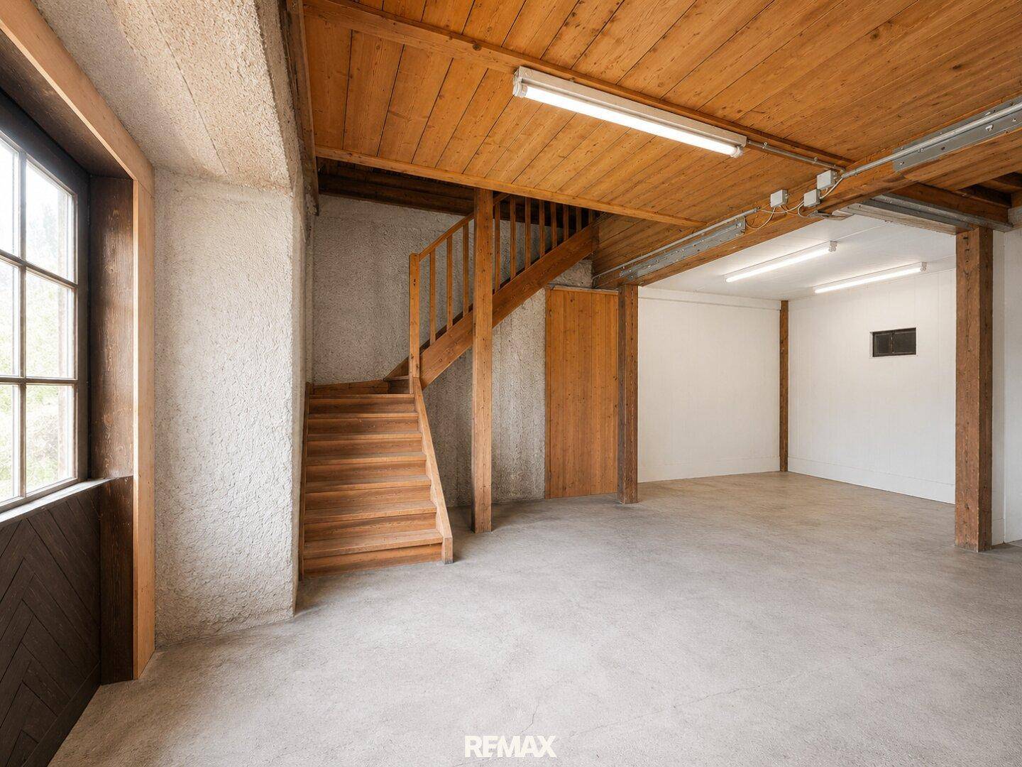 Heller Innenraum mit Holztreppe, Holzbalkendecke und großen Fenstern.